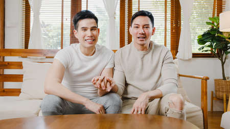 Young Asia gay couple propose at modern home, LGBTQ men happy smiling have romantic time while proposing and marriage surprise wear wedding ring in living room at house. Anniversary romantic concept.の写真素材