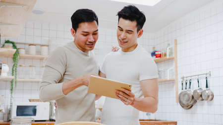 Young Asia gay couple propose at modern home, LGBTQ men happy smiling have romantic time while proposing and marriage surprise wear wedding ring in living room at house. Anniversary romantic concept.の写真素材