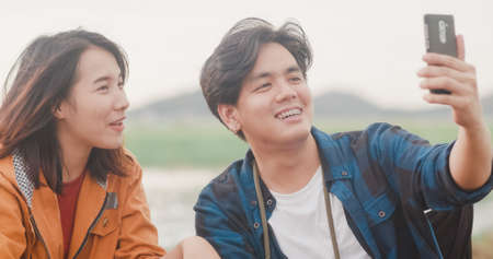 Young asia campers couple camping near seaside. Male and female traveler using smartphone vlog video and live in social media at campsite. Outdoor activity, adventure travel, or holiday vacation.の写真素材