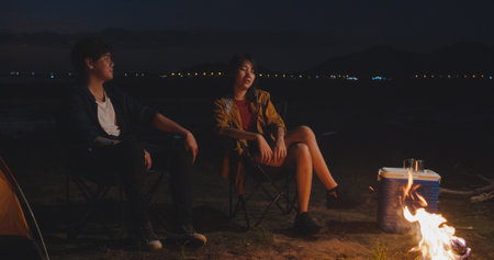 Young asia campers couple camping near seaside. Male and female traveler using smartphone vlog video and live in social media at campsite. Outdoor activity, adventure travel, or holiday vacation.の写真素材