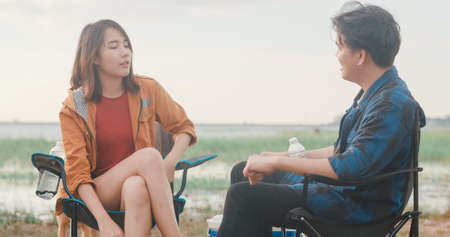 Young asia campers couple camping near seaside. Male and female traveler using smartphone vlog video and live in social media at campsite. Outdoor activity, adventure travel, or holiday vacation.の写真素材