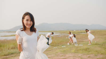 Portrait of young Asia lady volunteers help to keep nature clean up, looking at camera and smile with white garbage bags on the beach. Concept about environmental conservation pollution problems.の写真素材