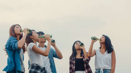 Group of Asia best friends teenagers lady dancing and drinking have fun salute toast of bottle beer enjoy party with happy moments together in campsite at night. Beautiful camping traveller concept.の写真素材