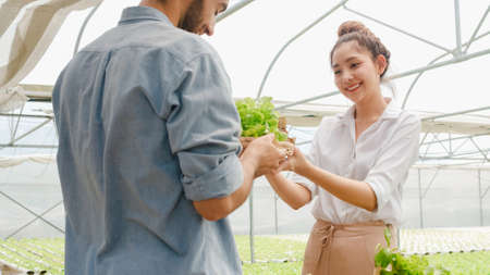 Young Asian businesswoman farmer hold tablet show performance of her organic farm to hispanic man buyer at greenhouse farm garden, New innovation technology in the cultivation concept.の写真素材
