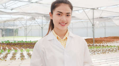 Close-up Happy Asian scientist woman looking at camera with smile hold document for research and development in organic vegetable at greenhouse farm garden, New technology in the cultivation concept.の写真素材