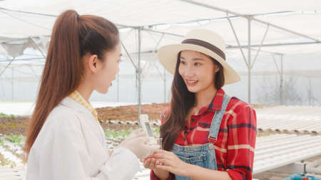Asian scientist woman test solution chemical inspection soil in organic farm and show result to the owner in greenhouse, Woman farmer in a garden, Concept for new technology in the agriculture.の写真素材