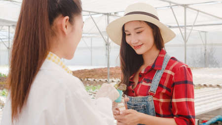 Asian scientist woman test solution chemical inspection soil in organic farm and show result to the owner in greenhouse, Woman farmer in a garden, Concept for new technology in the agriculture.の写真素材