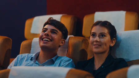 Attractive cheerful young caucasian couple laughing while watching film in movie theater. Lifestyle entertainment concept.の写真素材
