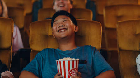 Handsome cheerful young asian boy laughing while watching film in movie theater. Lifestyle entertainment concept.の写真素材