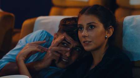 Attractive cheerful young caucasian couple kissing romantic moment while watching film in movie theater. Lifestyle entertainment concept.の写真素材