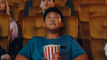 Handsome cheerful young asian boy laughing while watching film in movie theater. Lifestyle entertainment concept.の写真素材