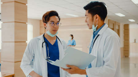 Asian doctors talk and discuss about patient's case in hospital. Asia men medical practitioner consult patient case, Pharmaceutical represent showing medical report, Hospital environment concept.の写真素材