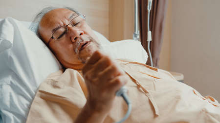 Little girl Asian granddaughter visiting hug sick senior grandfather hospitalized sit on hospital bed in patient room. Rehabilitation activity, health insurance, healthcare and medicine concept.の写真素材