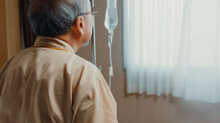 Little girl Asian granddaughter visiting hug sick senior grandfather hospitalized sit on hospital bed in patient room. Rehabilitation activity, health insurance, healthcare and medicine concept.の写真素材