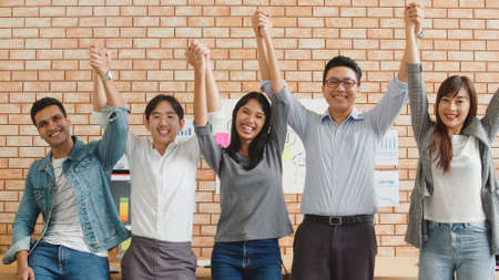 Portrait of successful creative businessman and businesswoman smart casual wear looking at camera and arms raise in modern office workplace. Diverse Asia male and female standing together at startup.の写真素材
