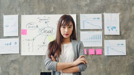 Portrait of successful beautiful executive businesswoman smart casual wear looking at camera and smile, arms crossed in modern office workplace. Young Asia lady stand in contemporary coworking space.の写真素材