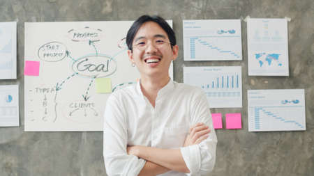 Portrait of successful handsome executive businessman smart casual wear looking at camera and smiling, arms crossed in modern office workplace. Young Asia guy standing in contemporary coworking space.の写真素材