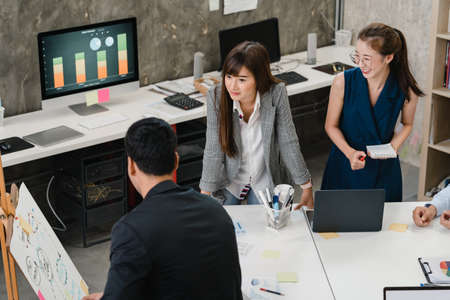 Asia businessmen and businesswomen meeting brainstorming ideas conducting business presentation project colleagues working together plan success strategy enjoy teamwork in small modern office.の写真素材