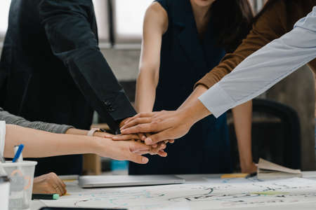 Asian businessmen and businesswomen meeting brainstorming putting hands up for new startup and giving strength motivation working together in modern creative office. Coworker teamwork concept.の写真素材