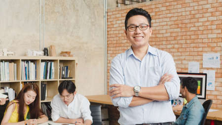 Portrait of successful handsome executive businessman smart casual wear looking at camera and smiling, arms crossed in modern office workplace. Young Asia guy standing in contemporary meeting room.の写真素材