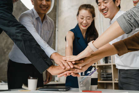 Asian businessmen and businesswomen meeting brainstorming putting hands up for new startup and giving strength motivation working together in modern creative office. Coworker teamwork concept.の写真素材