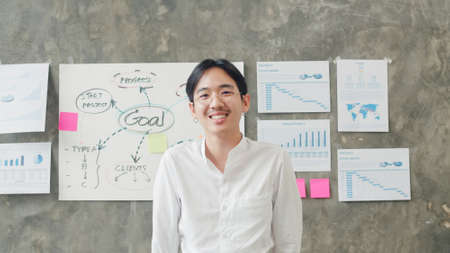 Portrait of successful handsome executive businessman smart casual wear looking at camera and smiling, happy in modern office workplace. Young Asia guy standing relax in contemporary coworking space.の写真素材