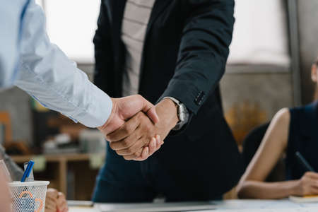 Multiracial group of young creative people in smart casual wear discussing business shaking hands together and smiling while sitting in modern office. Partner cooperation, coworker teamwork concept.の写真素材