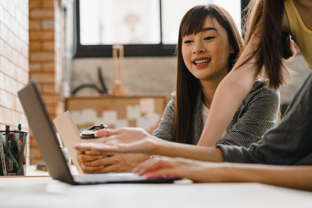 Group of Asia young creative people Japanese female boss supervisor teaching intern or new employee hispanic girl helping with difficult assignment in modern office. Coworker teamwork concept.の写真素材