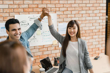 Multiracial group of young creative people in smart casual wear discussing business gesture hand high five, laughing and smiling together in brainstorm meeting at office. Coworker teamwork concept.の写真素材