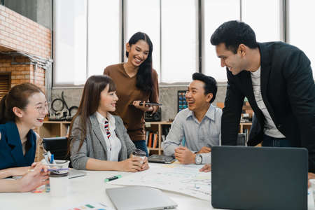 Multiracial group of young creative people in casual wear meeting brainstorming ideas about new paperwork project colleagues working together planning success strategy enjoy teamwork in small officeの写真素材