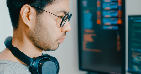 Closeup young adult Asia male freelance eyeglasses typing write prompt AI bot IT app program nomad, video game, terminal with coding, user interface, designer, big data center on desktop computer.の写真素材