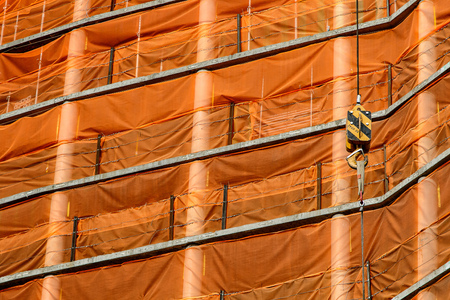 Crane cables and hook against orange mesh of a building under construction background.の写真素材