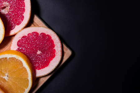 Oranges and red fruit on black wooden boards. Halves of juicy orange on black background. Orange fruit, citrus minimal concept. Top view, copy spaceの写真素材