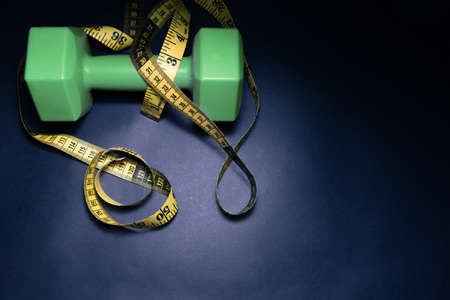 Dark sports concept. Sports equipment as dumbbells, expander with pink handles and centimeter tape on a dark black cement background, top view with a copy space.の写真素材