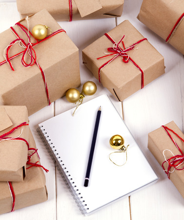list of gifts for Christmas. Drawing up a list of gifts. presents in kraft paper vintage white wooden background. pencil, notebook. vertical shotの写真素材