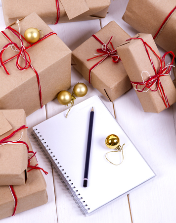 list of gifts for Christmas. Drawing up a list of gifts. presents in kraft paper vintage white wooden background. pencil, notebook. vertical shotの写真素材