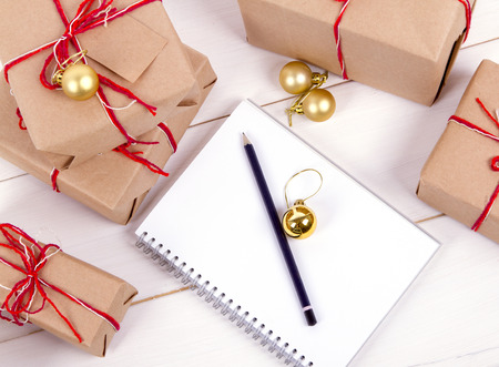 list of gifts for Christmas. Drawing up a list of gifts. presents in kraft paper vintage white wooden background. pencil, notebookの写真素材