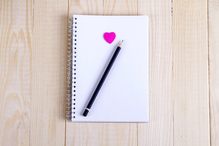 Open a blank Notepad and a pink heart on white wooden table. Valentine's day background. Free space for text. Top viewの写真素材
