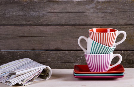 Colorful striped coffee cups on shelf against rustic old vintage wooden wall with copy spaceの写真素材