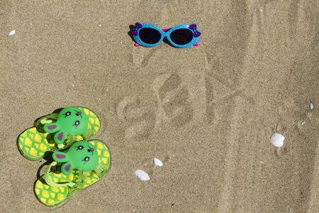 Children's slippers beach bunny on green sand and sunglassesの写真素材