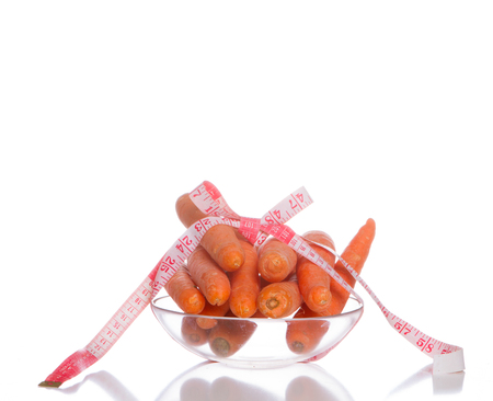 Carrot with a measure tape wrapped around over a white backgroundの写真素材