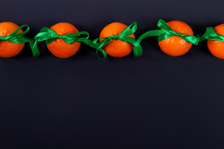row of tangerines on a black background tied with green satin ribbon as a giftの写真素材