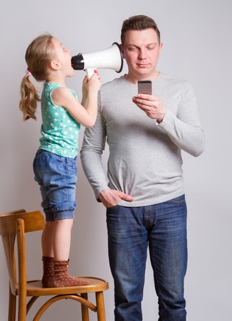 Father using smartphone ignoring his daughterの写真素材