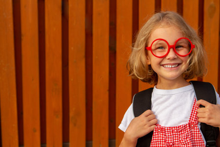 Happy cute clever girl in glasses with school bag