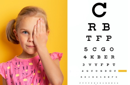 eyesight check. girl covering one eye with hand. eyesight check and health examinations.ophthalmology concept. Kid closing one eye with hand against alphabetical out of focus eye test chart in background.の写真素材