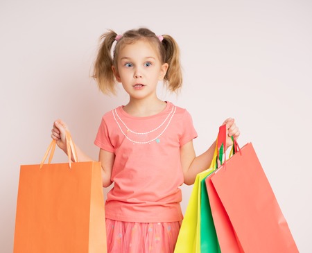 Portrait of excited surprised beautiful little child girl wearing dress, holding many shopping bags, isolated on light backgroundの写真素材