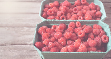 Fresh red raspberries in craft stalls, containers. on a wooden rustic old background. Top view of...