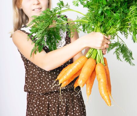 Cropped photo of teenager girl with a large armful of carrots with tops. Concept of healthy child nutritionの写真素材