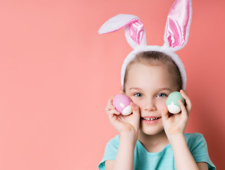 Little blonde child in headband with rabbit ears, dressed in blue t-shirt. She is smiling, showing...