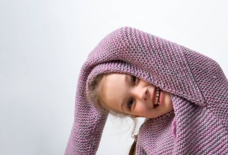 Joyful girl preschooler posing in large knitted lilac sweater, isolated on white. She is leaning aside with one hand above head, demonstrating long sleeve. Happy childhood, facial expression, kidsの写真素材
